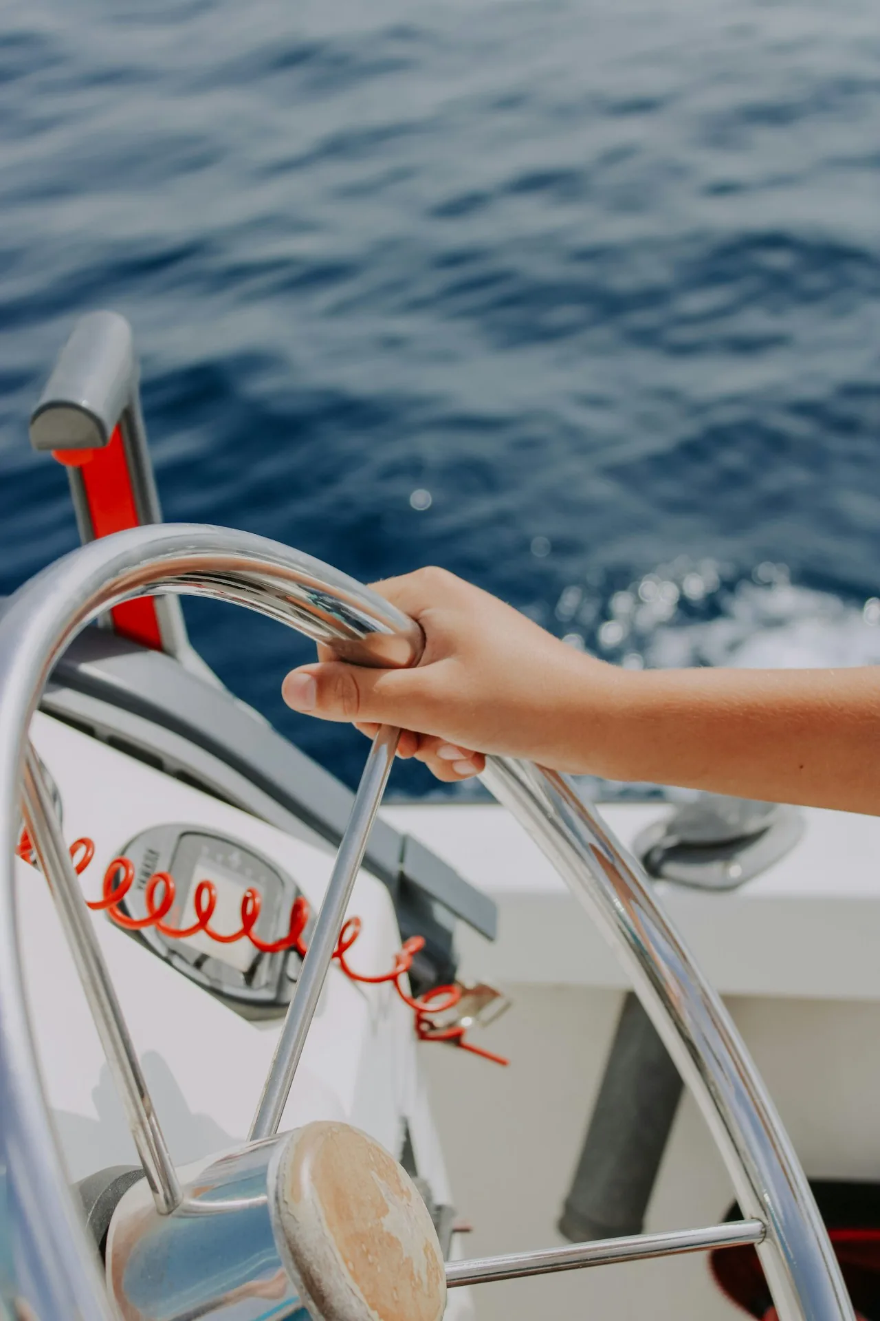 Main sur le volant inox d'un bateau à moteur, mer Méditerranée en arrière-plan